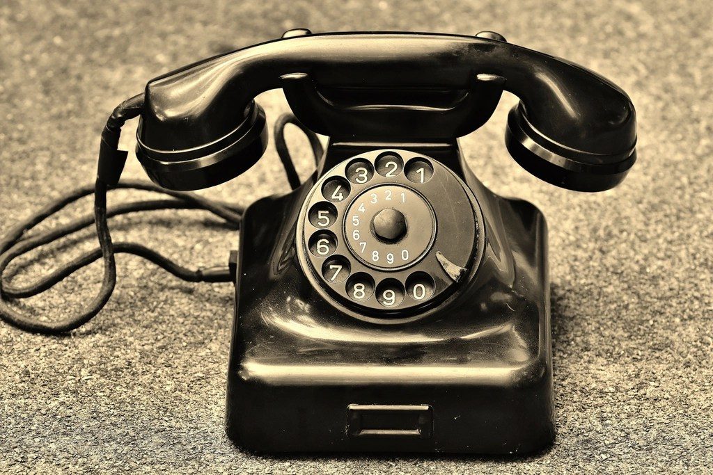 An old black dial telephone resting on gravel