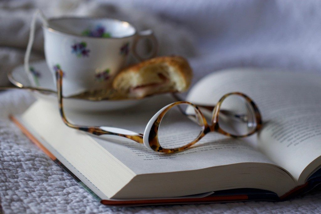 A pair of reading glasses resting on an open book beside a teacup