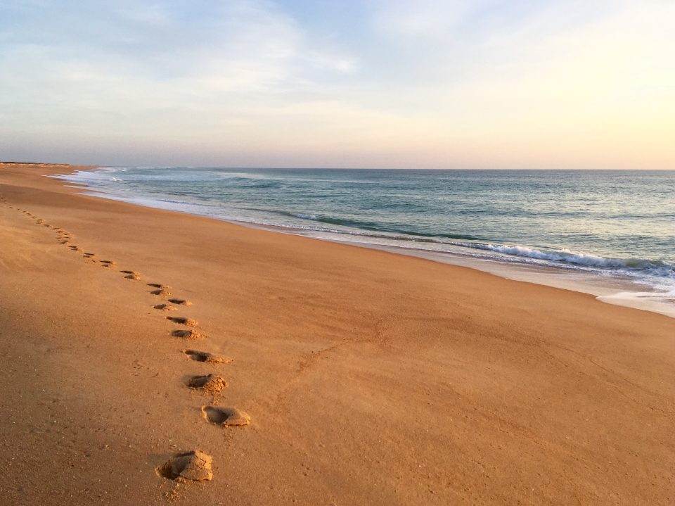 A line of footprints in smooth sand leading along a beach
