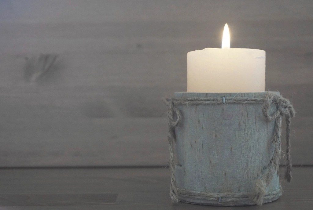 A single lit white candle on a small stand