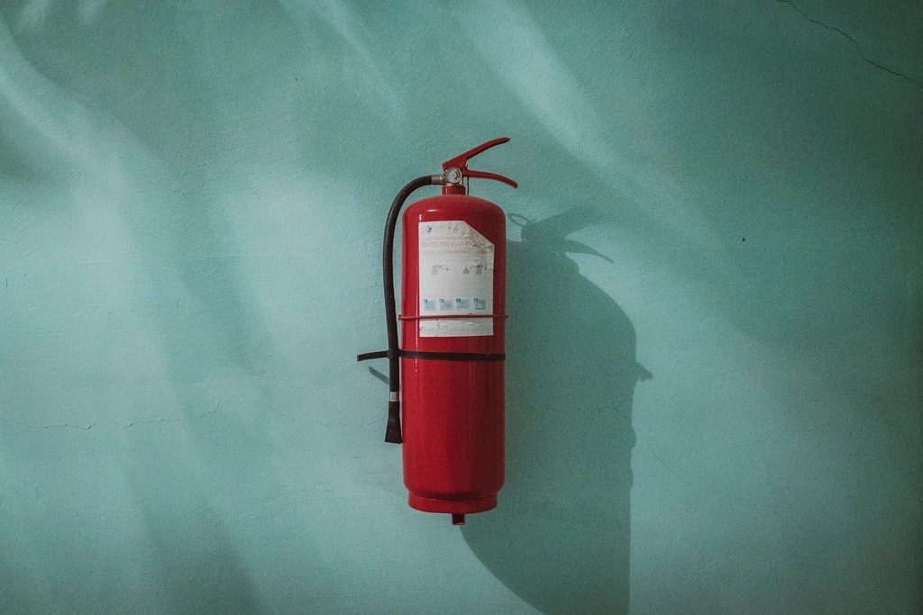 A red fire extinguisher mounted on a teal wall