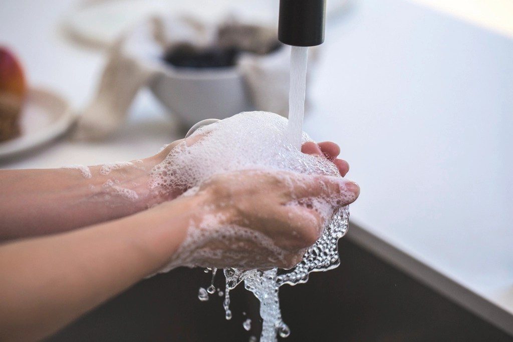 Two pairs of hands lathered with soap under a running tap