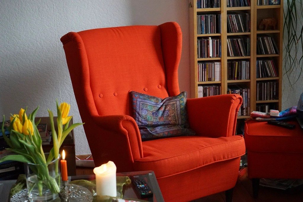 A red armchair in a living room with books, tulips and a lit candle