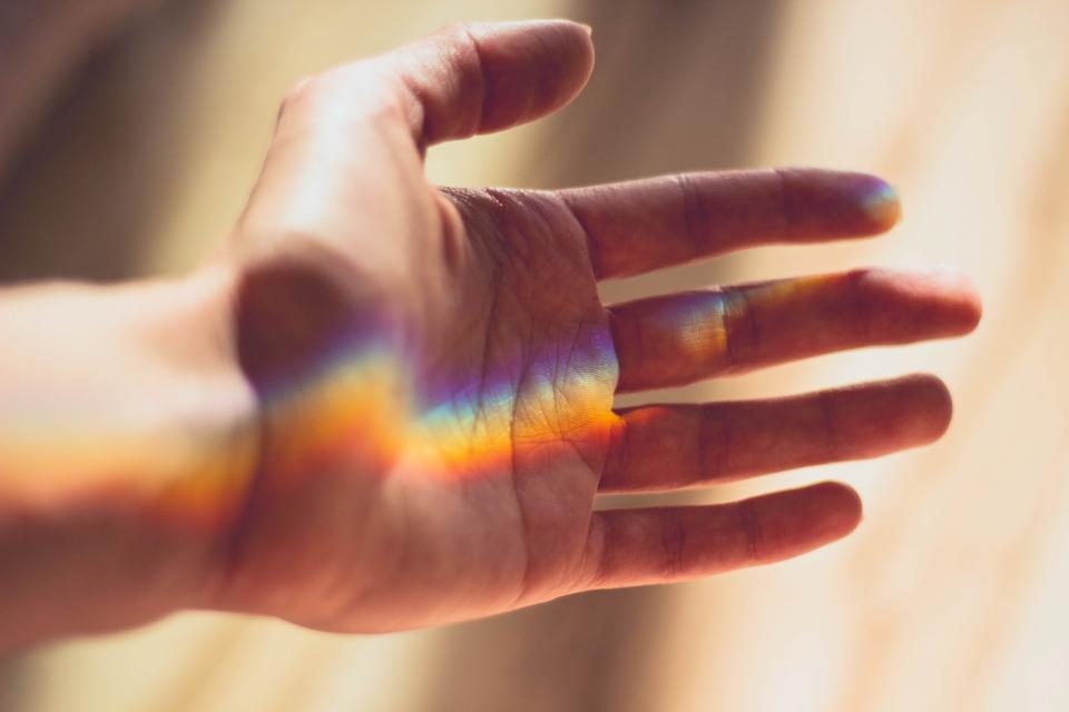 An open hand with a band of rainbow light falling across the fingers