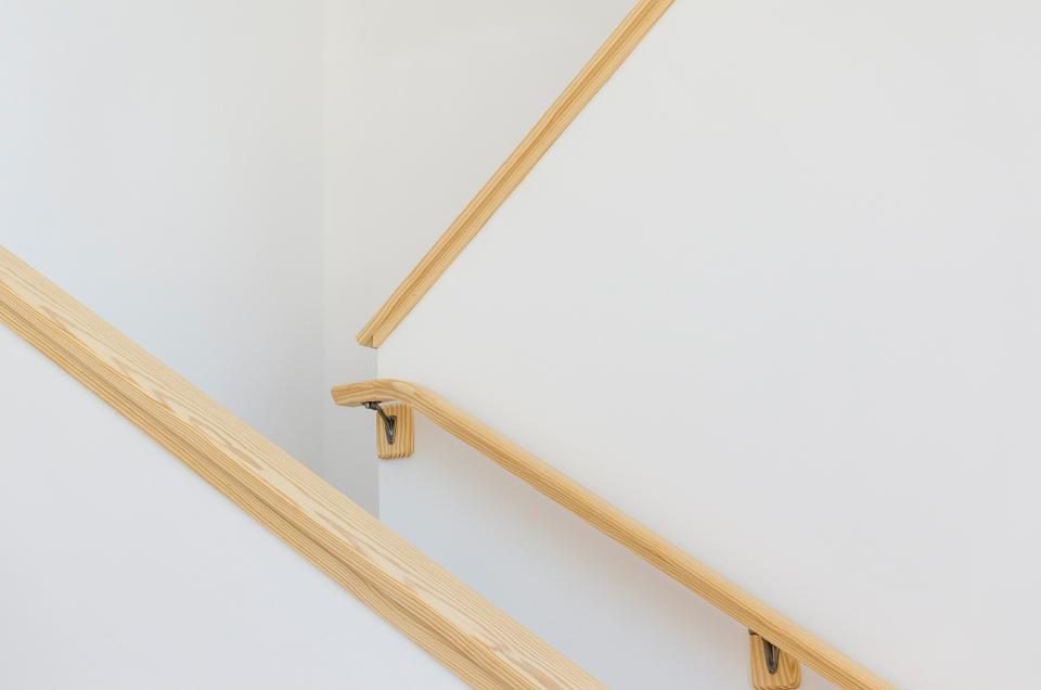 A wooden handrail running down a white stairwell