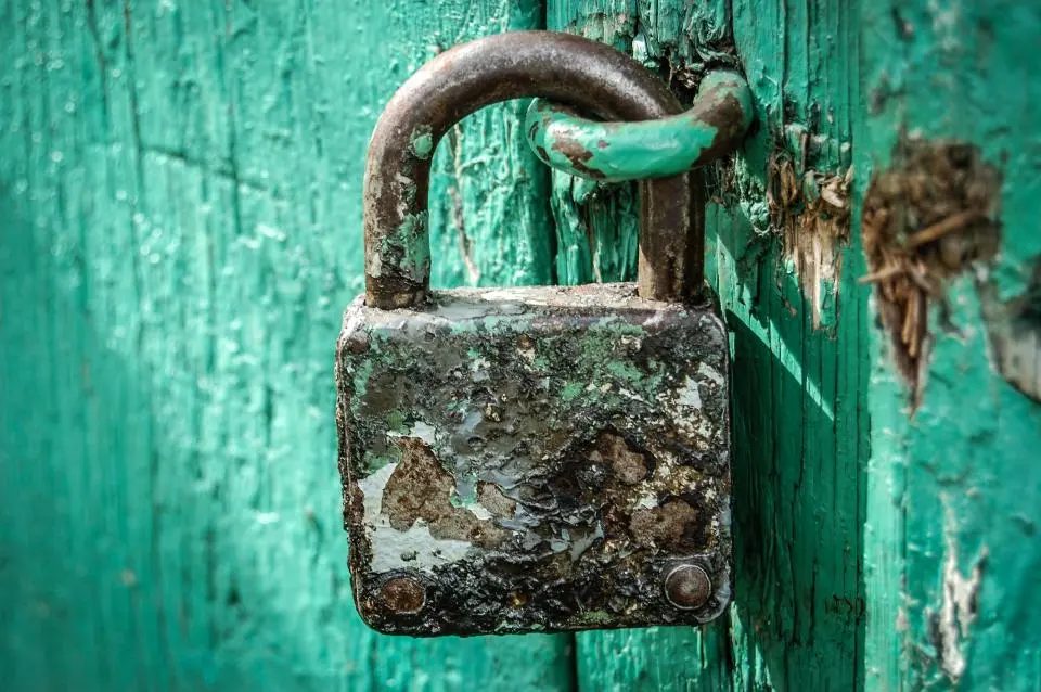 A weathered padlock on a turquoise wooden door