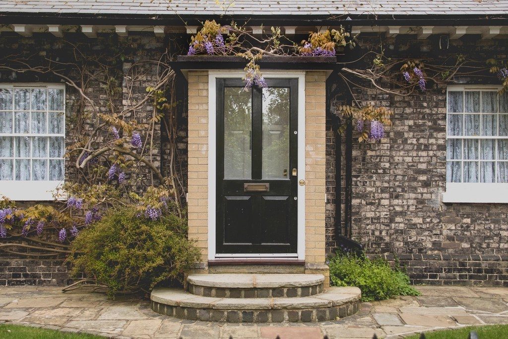 A front door with a stone step and a wisteria climbing the brick wall