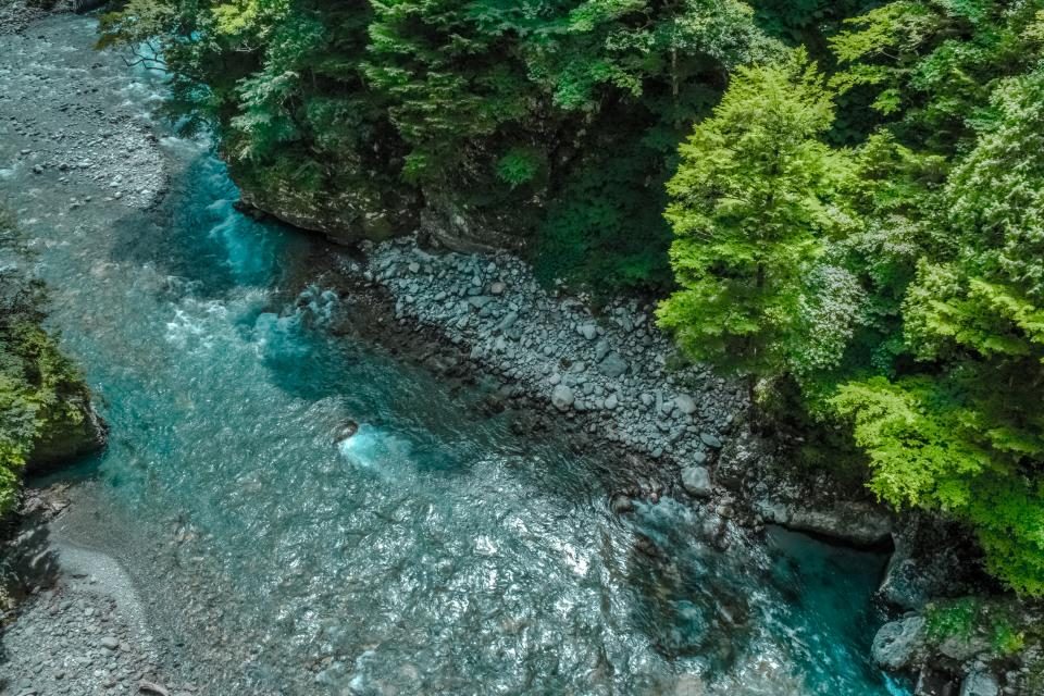 A clear turquoise river running between rocks and woodland, seen from above