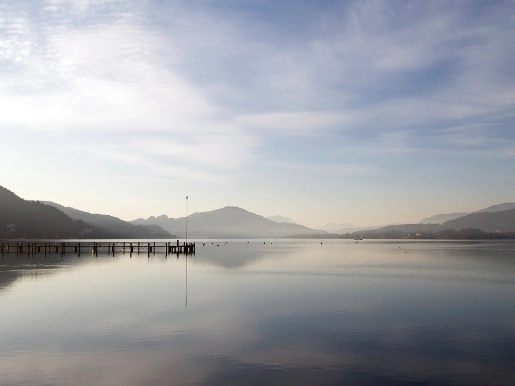 A calm lake with mountains in the distance under a soft sky