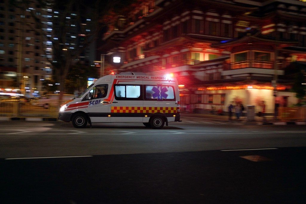 An ambulance with its lights on, driving through a city street at night